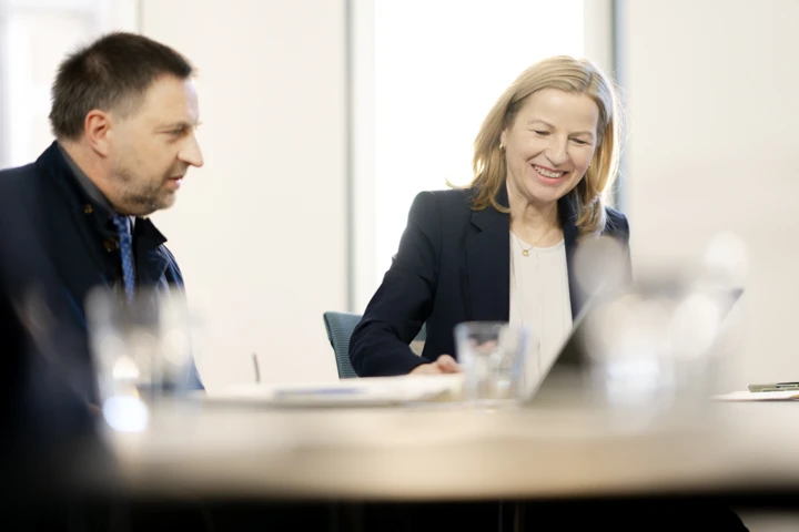 Zwei Personen sitzen am Besprechungstisch und lächeln.