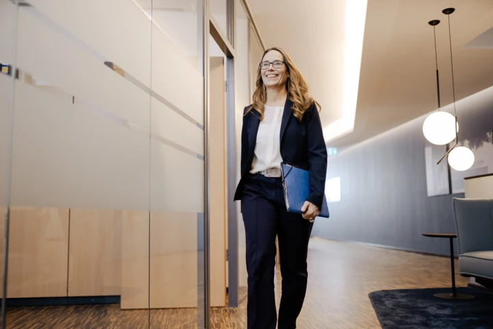 Eine Frau läuft lächelnd mit einem Ordner unterm Arm durch den Flur