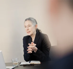 Ein Frau sitzt am Konferenztisch mit den Händen ineinandergeschlagen.