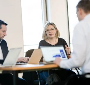 Drei Personen sitzen mit ihren Laptops aufgeschlagen an einem Konferenztisch