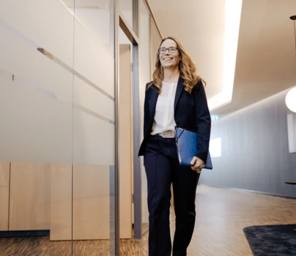 Eine Frau läuft lächelnd mit einem Ordner unterm Arm durch den Flur